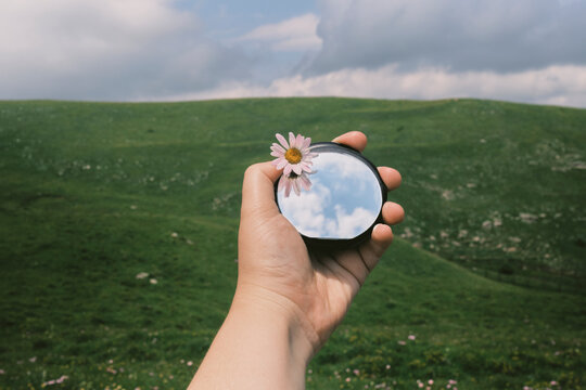 Holding a mirror with a flower outdoors on a green hill