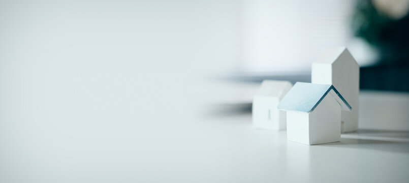 Miniature wooden house models on white desk with copy space, concept of real estate, property investment, housing market, home mortgage, and mortgage planning.