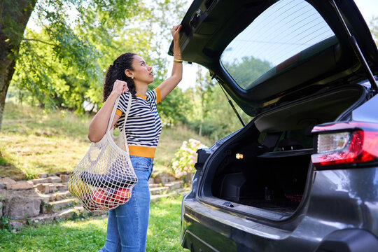 Woman opening car trunk holding reusable grocery bag