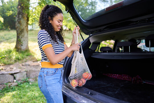 Woman loading fresh fruit into car trunk after shopping