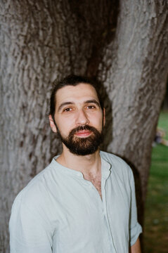 Man Stands Beside a Large Tree in a Garden During Daytime