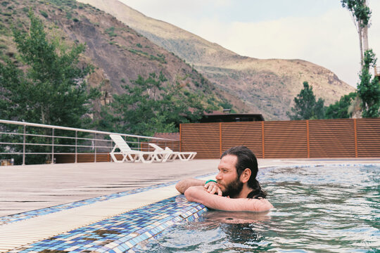 Man relaxing in pool surrounded by mountains in outdoor setting