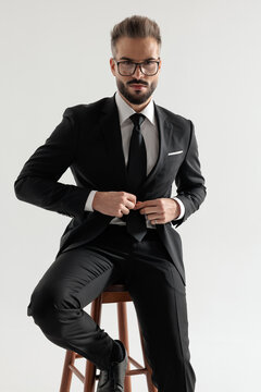 Professional man sitting on stool and buttoning suit jacket