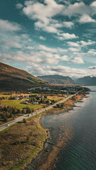 Vertical aerial view of a scenic coastal road winding past a village and mountains along the ocean in northern Norway with copy space in sky © Quality by Simon