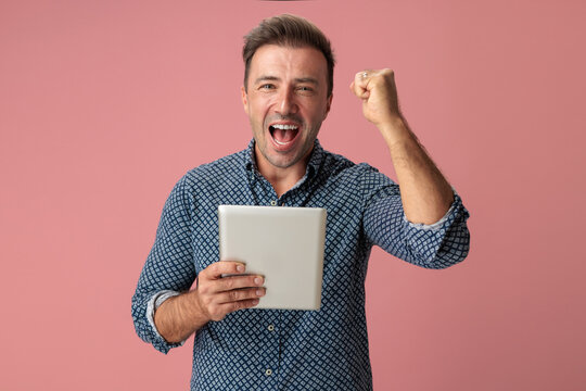 Excited man holding digital tablet and celebrating victory