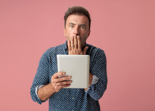 Surprised man covering mouth and holding digital tablet