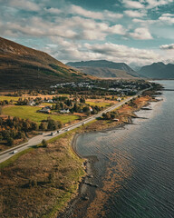 Vertical aerial view of a scenic coastal road winding past a village and mountains along the ocean in northern Norway with copy space in sky © Quality by Simon
