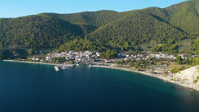 Aerial view of Neo Klima, a coastal village on Skopelos island, Greece, showing the settlement nestled between lush green hills and the clear blue waters of the Aegean Sea