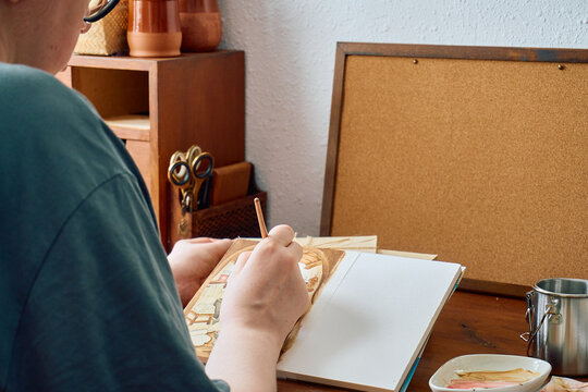 Artist painting watercolor illustration at wooden desk workspace