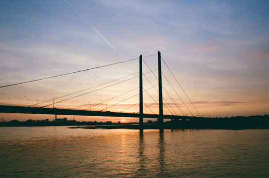 Cable-stayed bridge silhouette over river at sunset