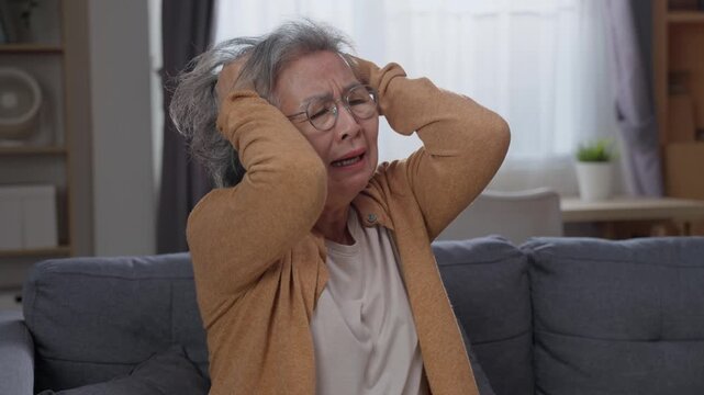 Distressed senior woman holding head feeling dizzy and weak in living room