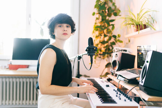 Young woman playing electronic keyboard in home music studio