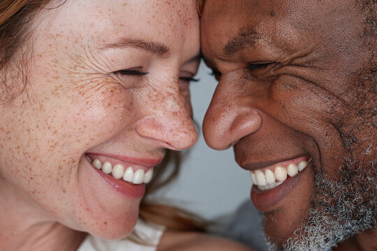 Smiling interracial couple touching foreheads in close up, joyful intimate moment showing teeth and facial detail, affectionate connection and warmth