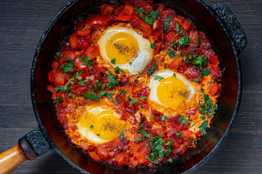 Traditional middle eastern shakshuka in cast iron skillet. Top view of traditional shakshuka with fried poached eggs in rich spicy tomato and bell pepper sauce topped with fresh parsley in pan
