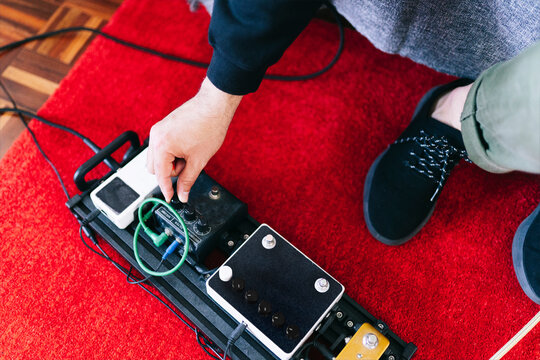 Musician adjusting guitar pedal effects in home studio