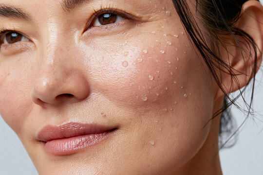 Dewy close up of Asian woman cheek with water droplets, natural skin texture, freckles, hydrated complexion and soft smile conveying freshness and confidence