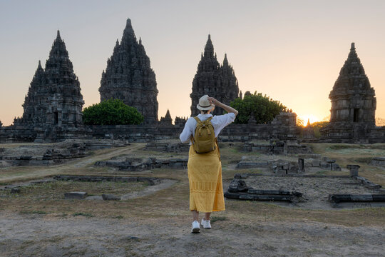 Woman tourist looking to a landmark at Prambanan temple during sunset.  woman with white and green dress and wearing hat.