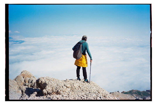 Hiker stands on mountaintop looking over clouds