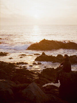 Man watches the sunset from a rocky coast