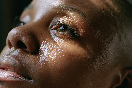 Moist skin close up portrait with warm light highlighting textured pores and eyelashes, conveying natural beauty and quiet confidence