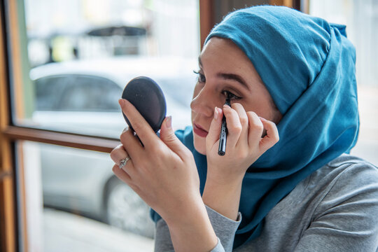 Woman applying eyeliner with mirror.