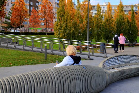 A woman relaxing on a bench in an autumn park an autumn cityscape, falling leaves