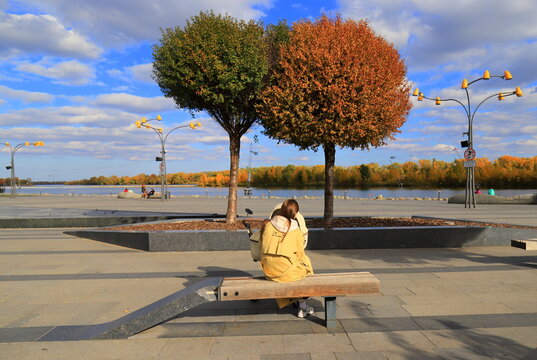 A woman relaxing on a bench in an autumn park an autumn cityscape, falling leaves
