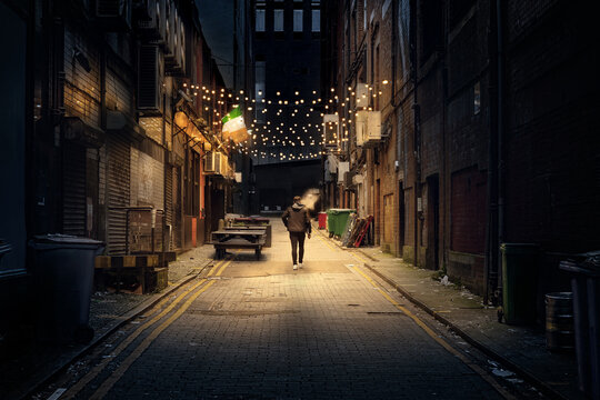 Person walking alone down brick alley at night with string light