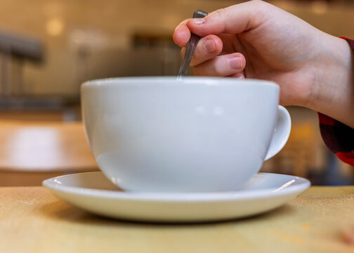 Hand stirring coffee in white ceramic cup on saucer in cafe