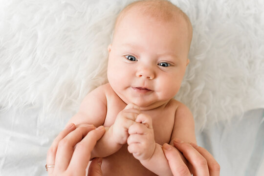 Mother holds the hands of baby 5-6 months old and plays at home, everyday scene of communication, care and motherhood