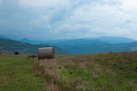 Hay bale on a green field with distant mountains under a cloudy sky, representing agriculture and rural life