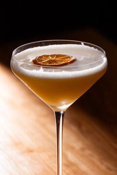 Beautiful Whiskey sour served up in a couple glass garnished with a dehydrated orange wheel with a warm wooden surface and background texture.