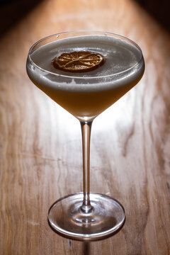 Beautiful Whiskey sour served up in a couple glass garnished with a dehydrated orange wheel with a warm wooden surface and background texture.