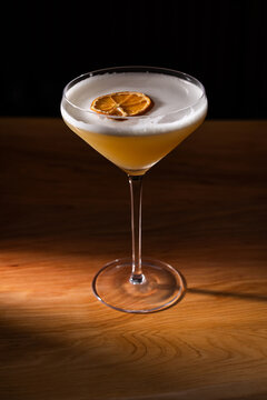 Beautiful Whiskey sour served up in a couple glass garnished with a dehydrated orange wheel with a warm wooden surface and background texture.