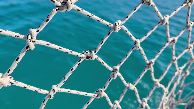 Sea View Through Yacht Railing Rope Net During Sailing. Yacht Rope Railing Net Overlooking the Blue Sea. Rope Safety Net Attached to Yacht Railing During Sea Journey.