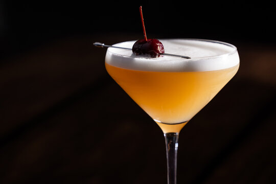 Beautiful Whiskey sour served up in a couple glass garnished with a dehydrated orange wheel with a warm wooden surface and background texture.