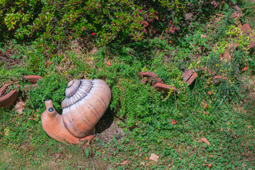 Decorative snail garden ornament among green groundcover and brick edging in sunny landscaped flower bed © Miroslav