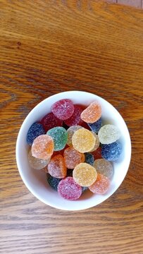 Colourful sugar coated gumdrops candies in a white bowl on a wooden table top view