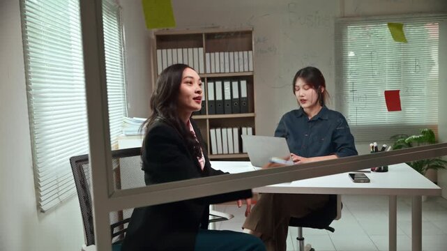 Two dynamic Asian colleagues collaborating on a new project, discussing strategy and brainstorming ideas together during a productive meeting in a modern corporate office environment