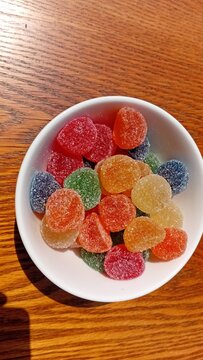  colourful sugar coated gumdrops candies in a white bowl on a wooden table top veiw