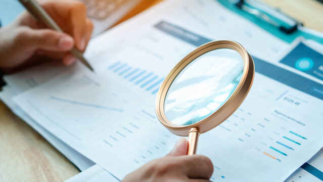 Accountant examines financial reports with a magnifying glass in an office. Business audit concept for document review, accounting analysis, compliance,  evaluation, and quality control.
