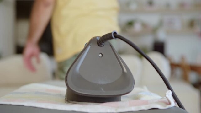 Close-up shot of a careless man leaving a hot iron resting on clothing. He walks out of the room, abandoning the appliance and highlighting a severe household fire hazard.