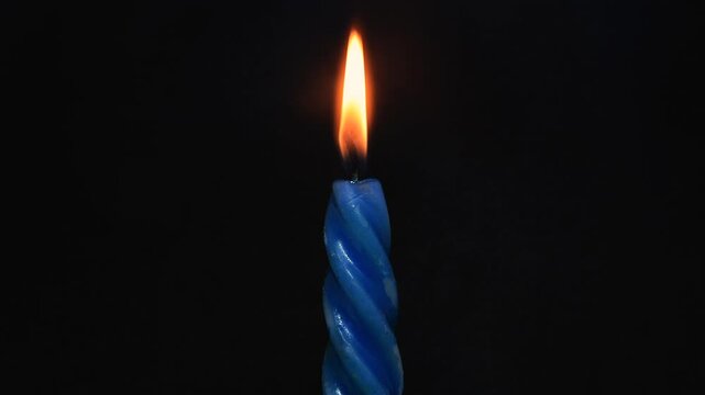  Relentless passage of time with time-lapse of a blue twisted candle burning with melting wax on black background.