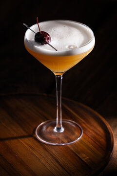 Beautiful Whiskey sour served up in a couple glass garnished with a dehydrated orange wheel with a warm wooden surface and background texture.