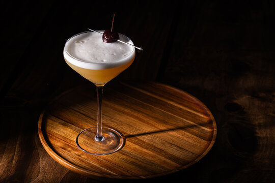 Beautiful Whiskey sour served up in a couple glass garnished with a dehydrated orange wheel with a warm wooden surface and background texture.