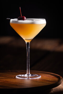 Beautiful Whiskey sour served up in a couple glass garnished with a dehydrated orange wheel with a warm wooden surface and background texture.