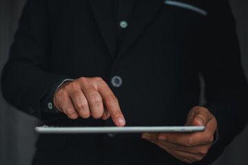 Businessman in dark suit holding slim digital tablet and touching touchscreen for mobile business management and paperless workflow © MarkFinal