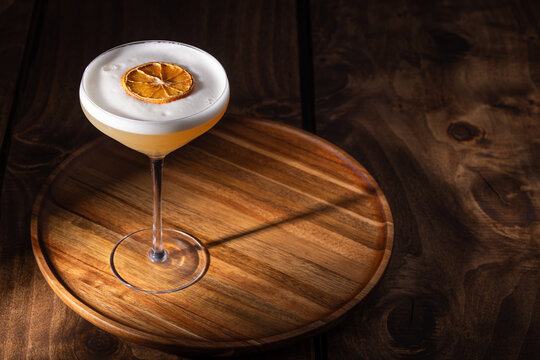 Beautiful Whiskey sour served up in a couple glass garnished with a dehydrated orange wheel with a warm wooden surface and background texture.