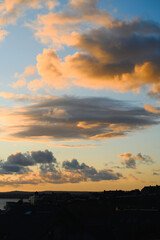 Obraz premium Glowing sunset clouds drift above coastal rooftops in Saint Ives, Cornwall, England, with warm evening light, layered sky and distant shoreline view.