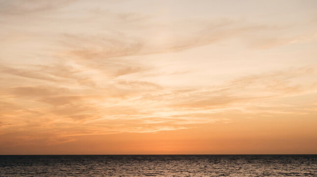 Tranquil ocean horizon view with warm orange sky and wispy clouds during sunset or sunrise